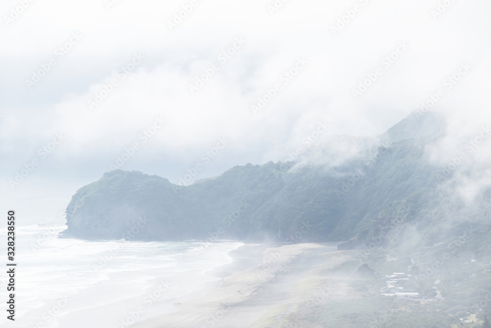 Aerial view of Te Waha Point and Kohunui Bay at North Piha beach covered in thick fog