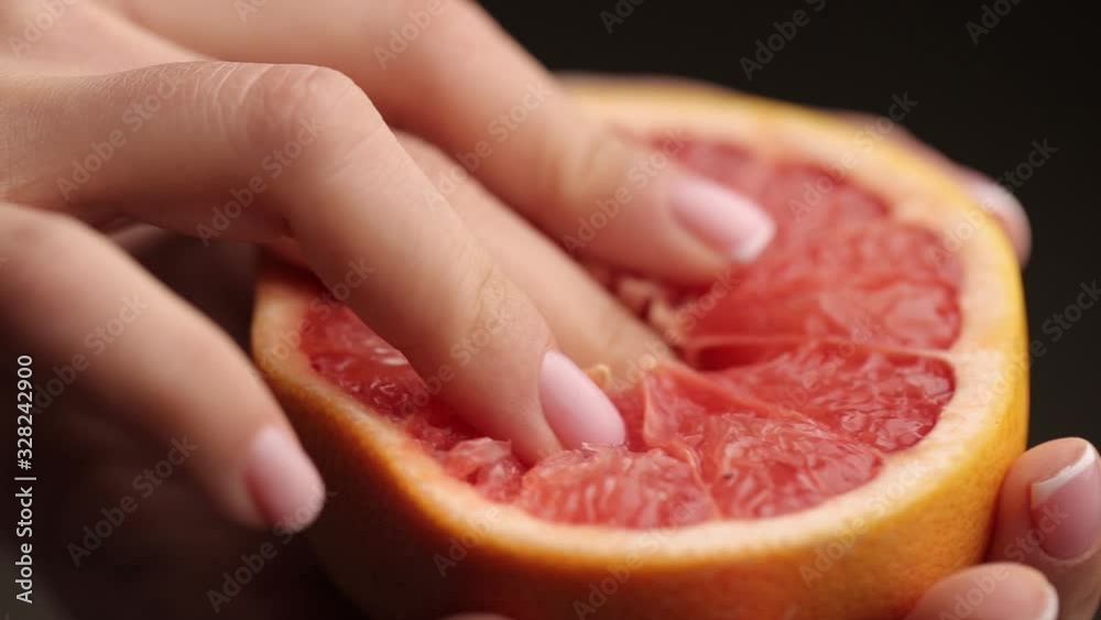 Blurred frame. Female hand close-up crushes grapefruit on a black background. Studio isolated background.