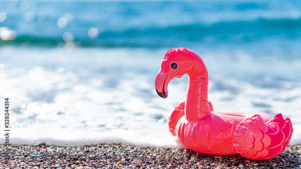 Fototapeta Inflatable pink flamingos on beach with white foam of sea wave. Summer, vacation, swimming, beach resort concept with pink flamingo. Banner. Copy space for text or design.