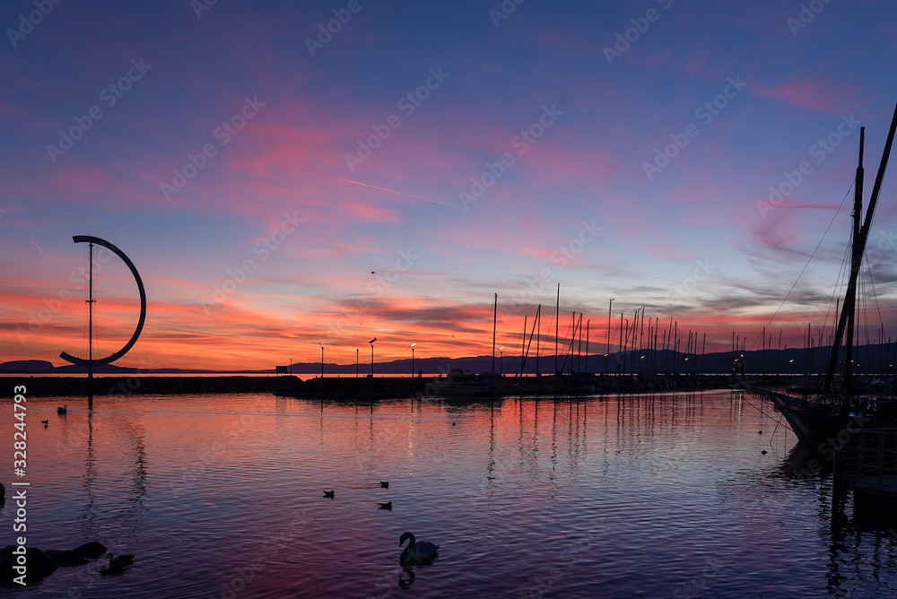 PORT OF OUCHY IN THE SUNSET WITH BLUE SKY, ORANGE CLOUDS AND CALM LAKE