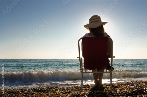 a young girl sitting on a chair watching the sunset at the beach