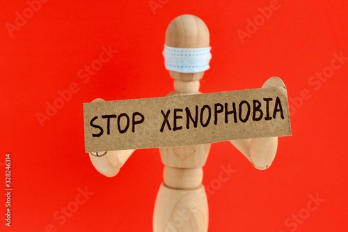 Cardboard sign with text stop xenophobia in the hands of a wooden doll or mannequin in a medical mask. Concept of anti racism, anti xenophobia, the social situation around the Coronavirus or Covid-19.