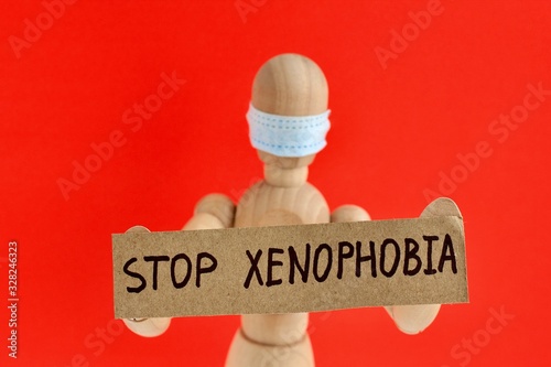 Cardboard sign with text stop xenophobia in the hands of a wooden doll or mannequin in a medical mask. Concept of anti racism, anti xenophobia, the social situation around the Coronavirus or Covid-19. photo