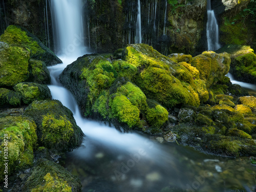 Cascada de agua en arroyo y rocas con musgo verde.