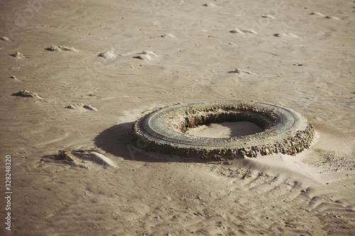 Old car tire covered with sand after low tide