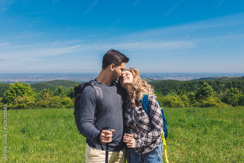 Smiling couple enjoying hiking together in nature standing on the top of the hill.