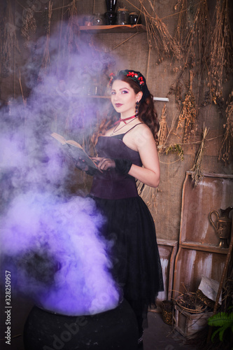Fototapeta Naklejka Na Ścianę i Meble -  A young witch with a book in her hands cooks a potion in a large black cauldron, emitting magical purple smoke.