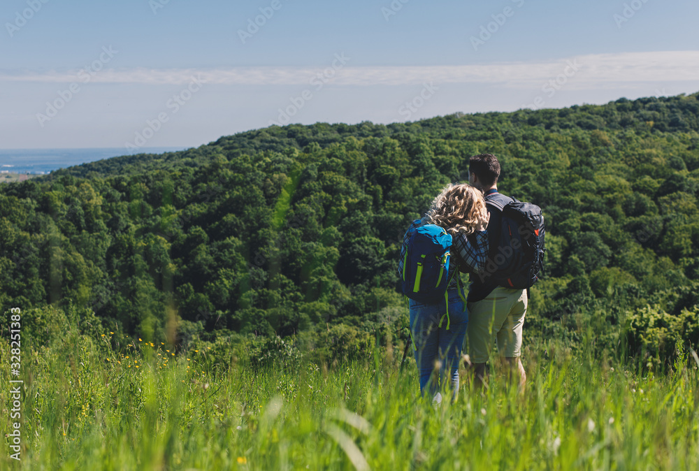 Smiling couple enjoying hiking together in nature standing on the top of the hill.