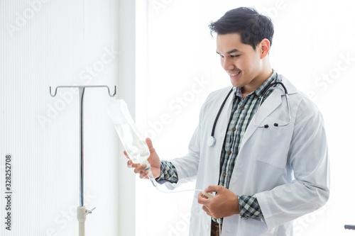 Portrait of Asian Young man doctor therapeutic advising smiling face with stethoscope holding with saline bottle with in hospital background.