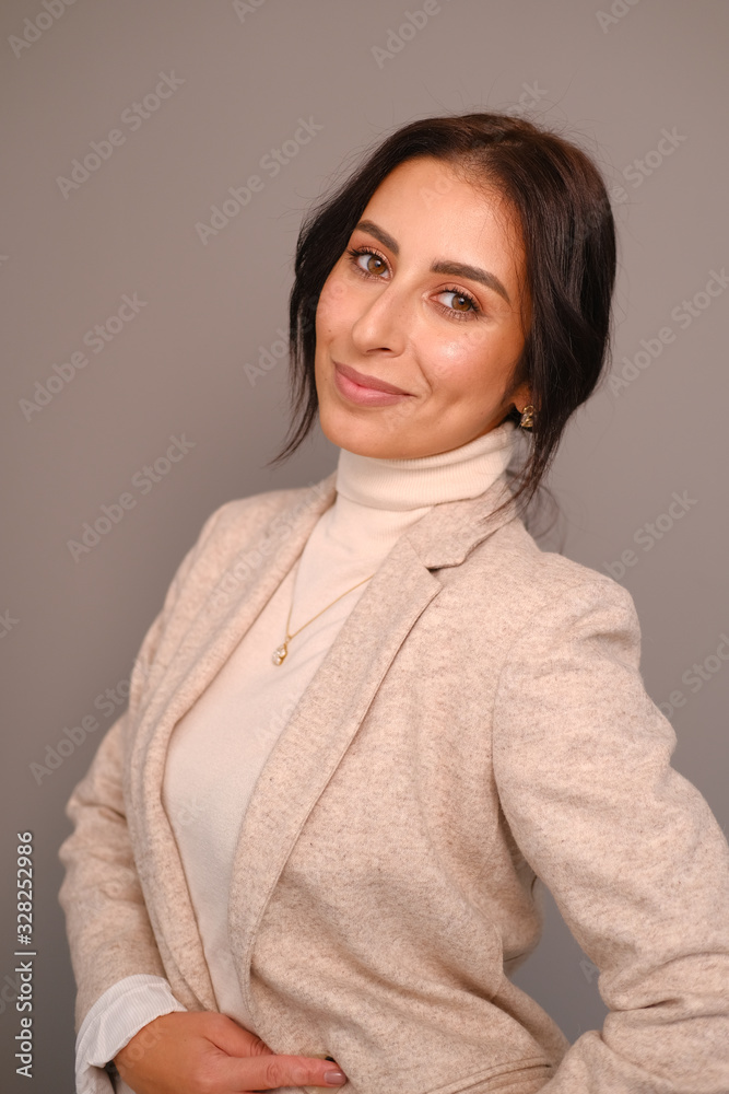 Portrait of a smiling mid-aged business woman in a light milk-colored trouser suit and turtleneck against a light wall. Portrait of a smiling mid-aged business woman in a light milk-colored trouser suit and turtleneck against a light wall.
