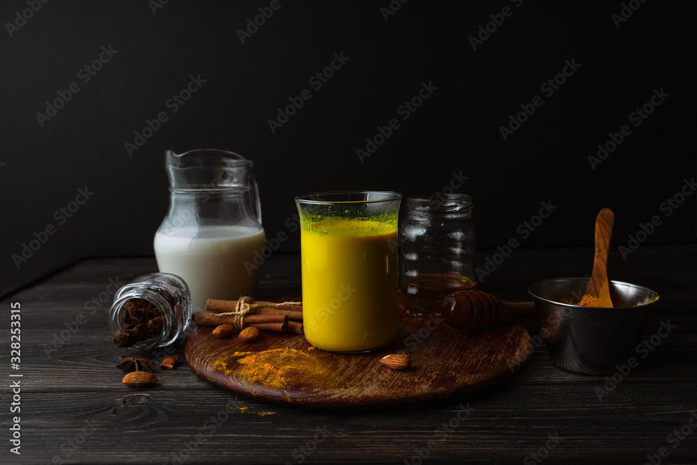 Vegan turmeric latte in a glass, almond milk, spices on dark rustic background, closeup view Vegan turmeric latte in a glass, almond milk, spices on dark rustic background, closeup view