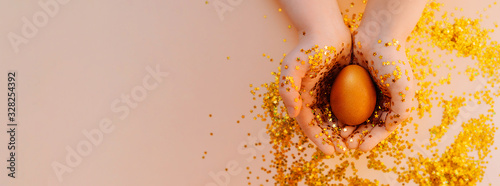 light skin hand in gold spangles in the form of stars firmly hold a Golden Easter egg on a pink background with sequins. Happy Easter flat lay mockup banner