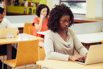 Multiethnic adult students working on computers in public library. People sitting at desks and using laptops. Public place and education concept