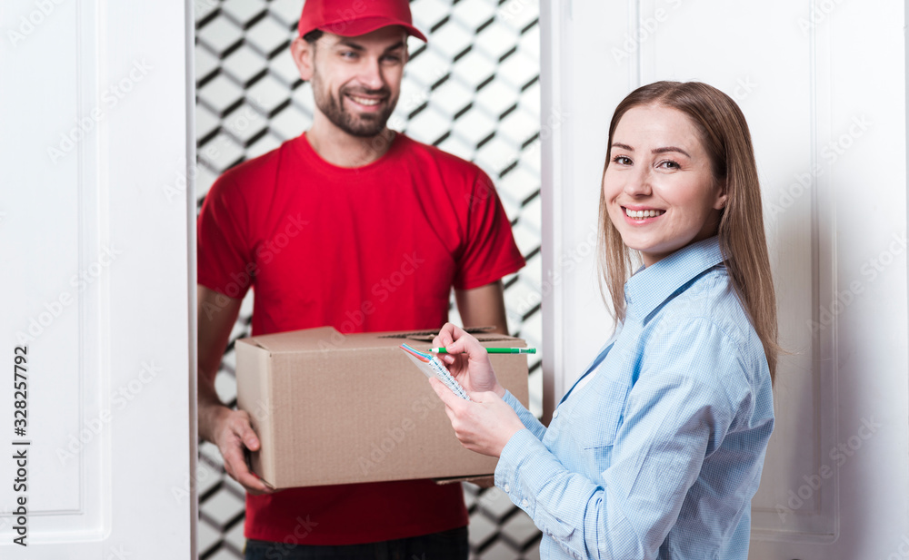 Fototapeta premium Woman receiving a package from the courier and signing the forms