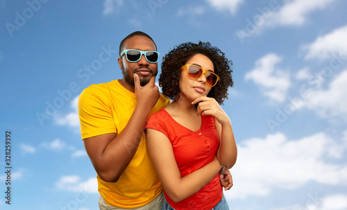 people, accessories and summer concept - african american couple in sunglasses thinking over grey background