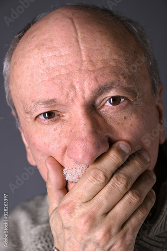Sad lonely elderly man posing in studio over gray background