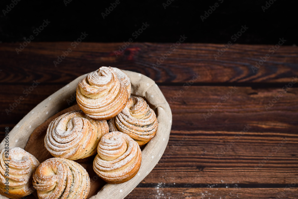 Fototapeta premium Delicious modern cruffins are made from puff croissants in the form of a muffin. cruffins with a wooden basket on a dark wooden background, sprinkled with powdered sugar and raspberries. Copy space