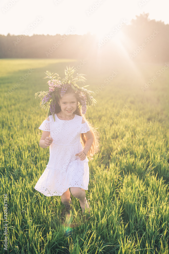 A girl in a white dress and a wreath of flowers runs on a green field A girl in a white dress and a wreath of flowers runs on a green field