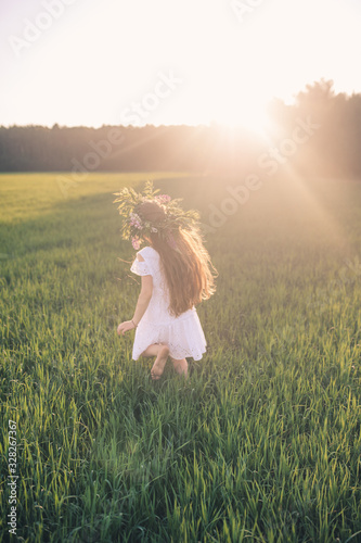 A girl in a white dress and a wreath of flowers runs on a green field