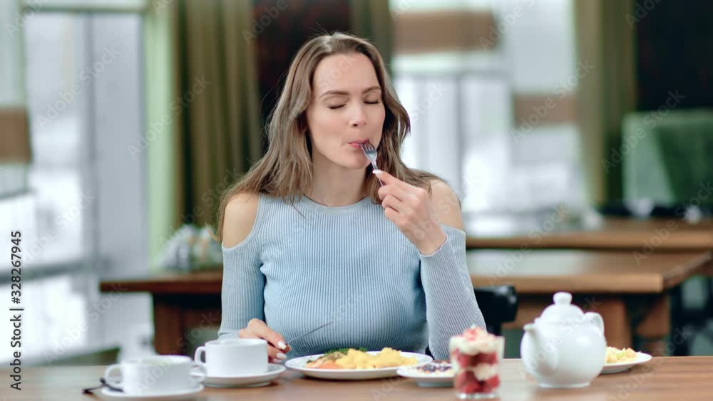 Portrait of smiling woman eating fresh tasty food posing at cafe table. Medium shot on RED camera Portrait of smiling woman eating fresh tasty food posing at cafe table. Medium shot on RED camera