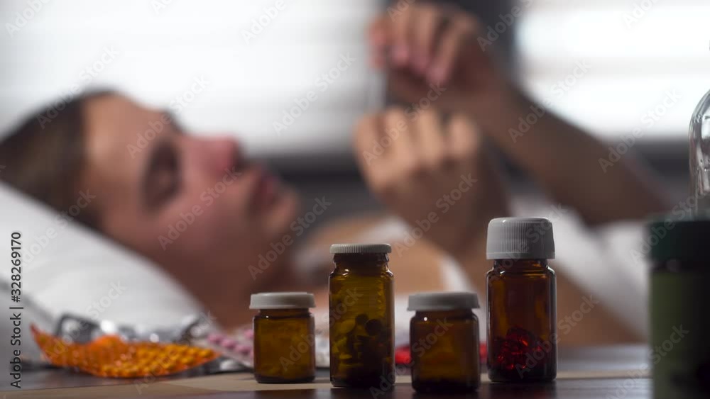 Pile of medicines, pills in glass containers on the front, foreheads checks the temperature on the background Pile of medicines, pills in glass containers on the front, foreheads checks the temperature on the background
