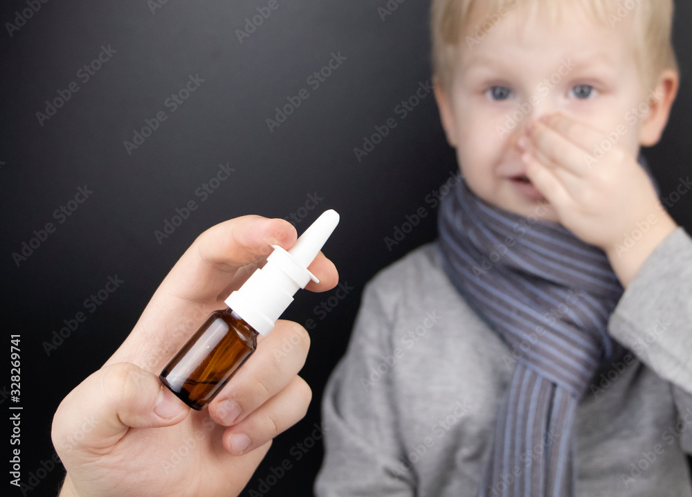 Obraz premium A runny nose is treated with a medicine from a nasal spray. Nasal drops on a black background. Concept for treating a baby cold or viral infection.