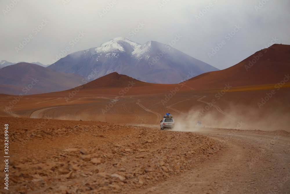 Bolivia desert in Potosi province, Andes highlands. Off road vehicle 4x4 crossing the arid land in the desert. Wild scenery with arid  soil, mountains and cloudy sky. Off road adventure.