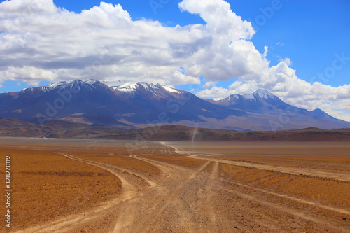 Bolivia desert in Potosi province, Andes highlands. Dust roads crossing the arid land in the desert. Wild scenery with arid soil, mountains and cloudy sky. Off road adventure.
