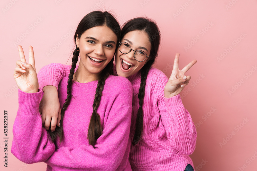 Image of two happy teenage girls smiling and gesturing peace fingers Image of two happy teenage girls smiling and gesturing peace fingers