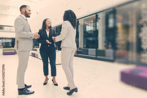 Cheerful business partners happy to see each other. Business man and women standing in office hall, shaking hands with each other, talking and smiling. Successful partnership concept
