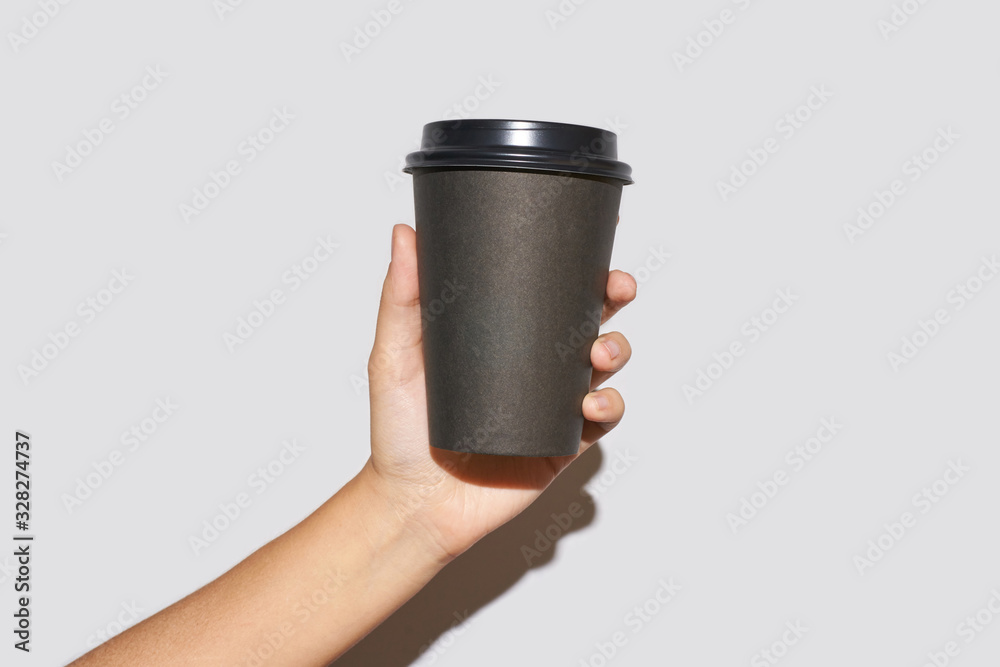 Girl hand hold coffee plastic cup. Grey background with copyspace. Female arm holding paper glass. To go, away. No ecology. Hard shadows. Horizontal banner Girl hand hold coffee plastic cup. Grey background with copyspace. Female arm holding paper glass. To go, away. No ecology. Hard shadows. Horizontal banner