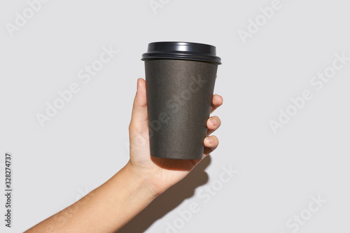 Girl hand hold coffee plastic cup. Grey background with copyspace. Female arm holding paper glass. To go, away. No ecology. Hard shadows. Horizontal banner