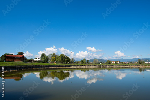 Paesaggio con lago di campagna e riflesso del cielo e delle nuvole sull'acqua con case e alberi