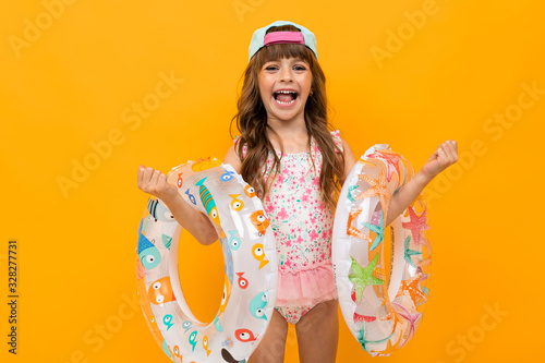 Beautiful little girl in swinsuit holds a rubber rings isolated on yellow and orange background photo