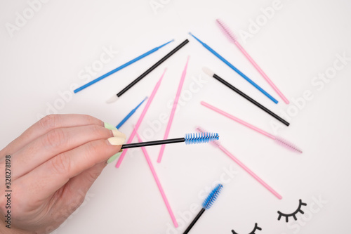 Top view of flatlay from eyelash extension tools. Female hand holds colored brushes for combing cilia.