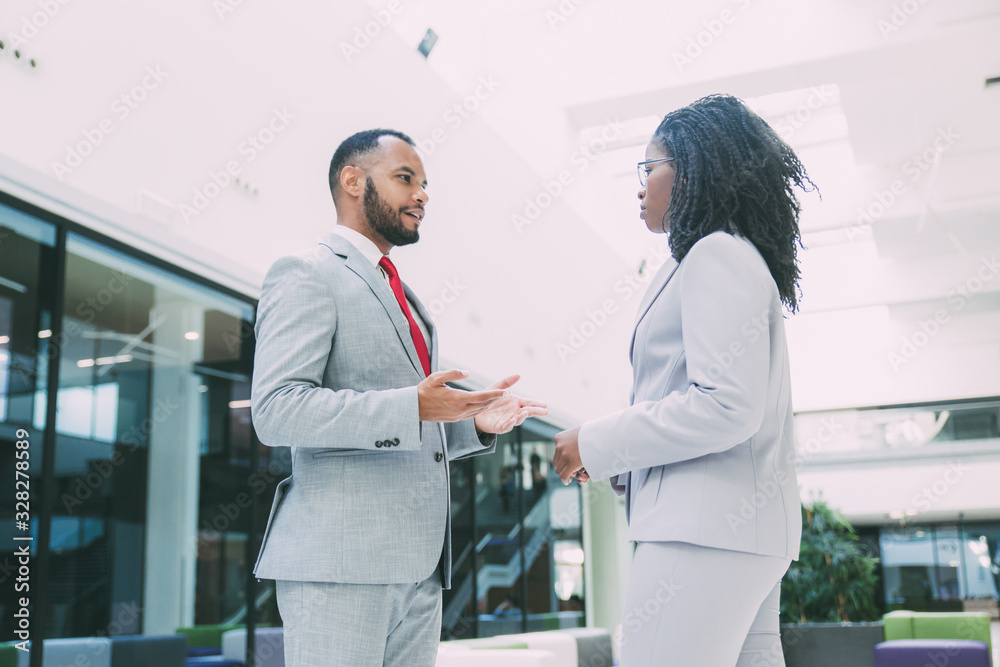 Fototapeta premium Confident multiethnic business couple meeting in office hall. Business man and woman standing and talking to each other. Corporate conversation concept