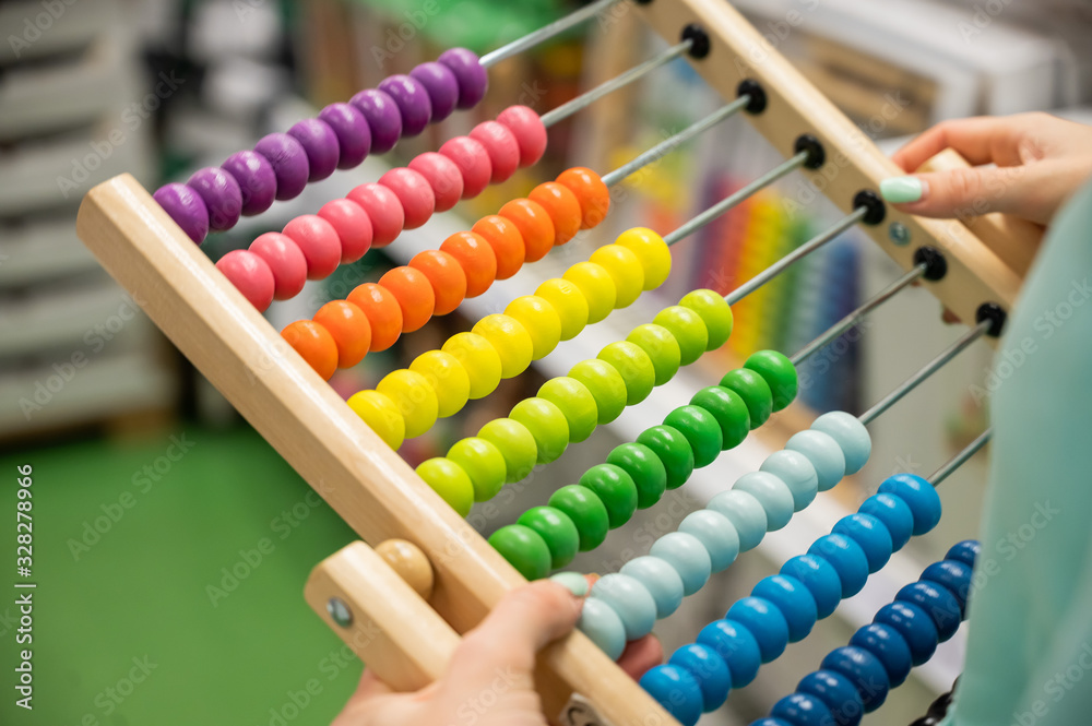 Closeup female hand calculating with balls on wooden rainbow abacus for number calculation. The concept of learning arithmetic for preschoolers. Closeup female hand calculating with balls on wooden rainbow abacus for number calculation. The concept of learning arithmetic for preschoolers.