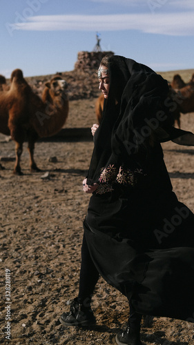 beautiful woman national eastern clothes black color,veil,hijab,abaya ornament her head,portrait steppes camels,strong wind,desert,wildlife,well,decoration,caucasian,slow ,sun