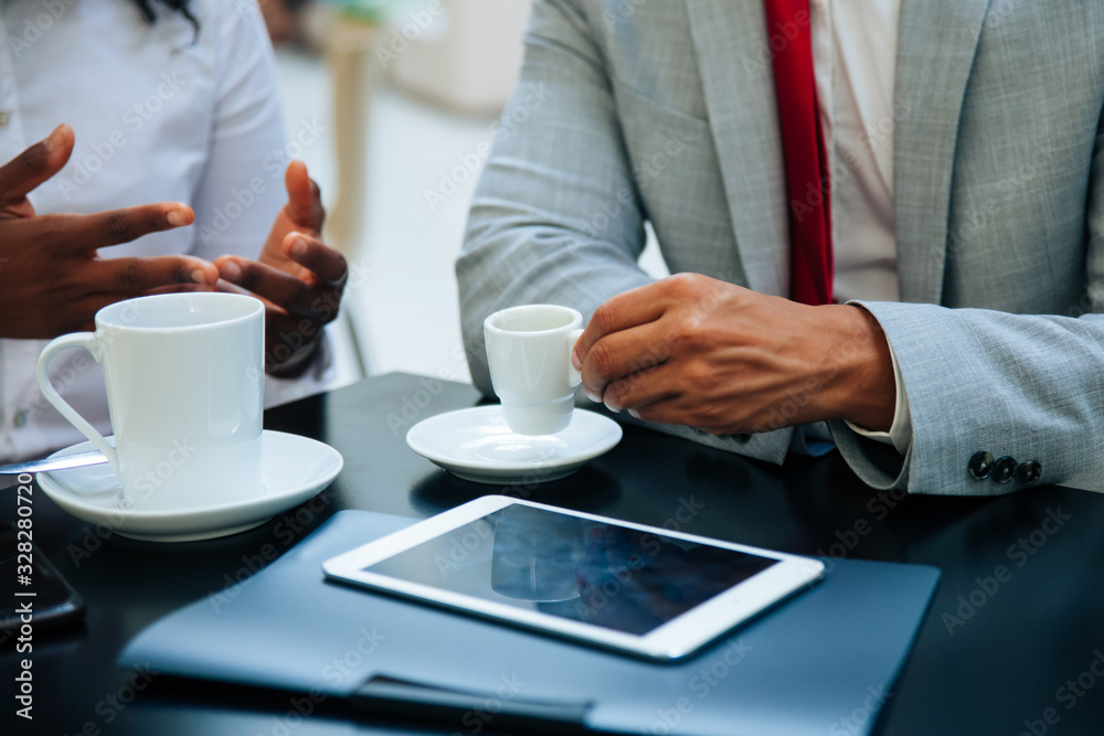 Business partners discussing work issues over cup of coffee. Hands of business people sitting at table with tablet in cafe, drinking coffee, gesturing. Coffee break concept