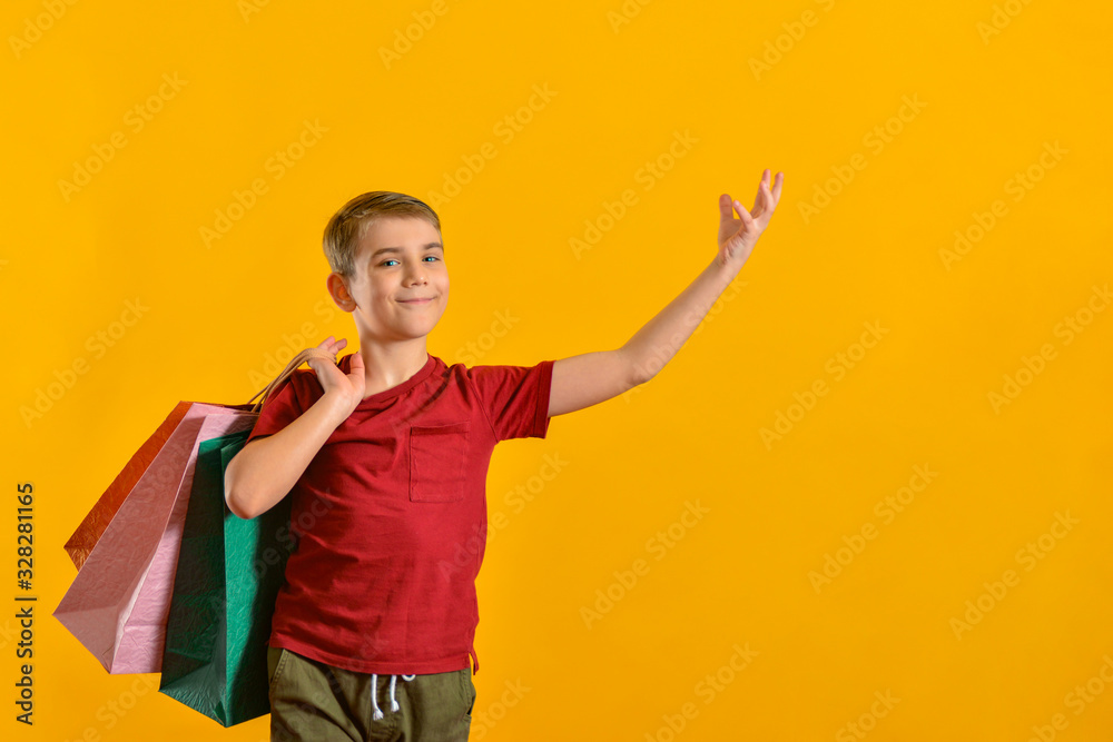 A joyful and happy buyer with colored bags in his hand shows his positive emotions from purchases. Baby with purchases on a yellow background. A joyful and happy buyer with colored bags in his hand shows his positive emotions from purchases. Baby with purchases on a yellow background.