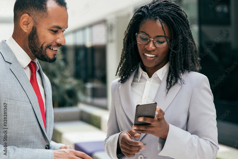 Excited happy colleagues looking at mobile phone screen together. Business woman showing smartphone content to male colleague. Wireless communication concept Excited happy colleagues looking at mobile phone screen together. Business woman showing smartphone content to male colleague. Wireless communication concept