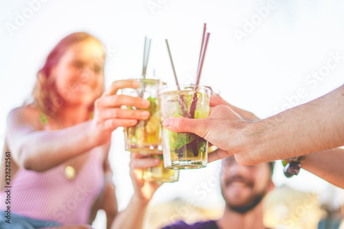 Group of friends toasting with cocktails on the beach kiosk. Young friends having fun cheering outdoors, focus on the hand. Happiness and togetherness lifestyle concept.