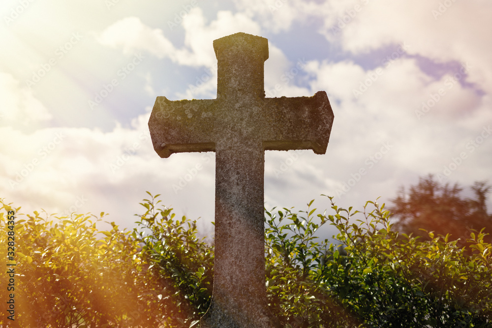 grey grave stone cross standing alone in Cemetery, blue sky background, daylight, in sunlight as a symbol of strength, truth and faith