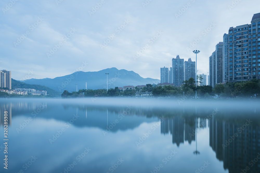 Fototapeta premium In the early morning of the city, the sky is full of rosy clouds, and the advection fog flows around the river, hazy and beautiful