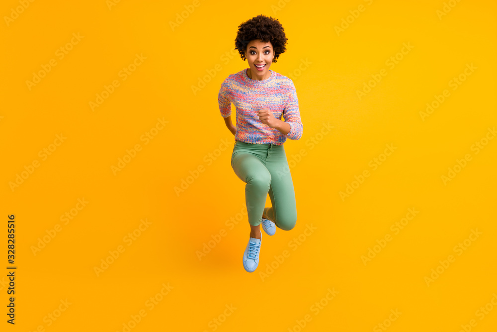 Full size photo of crazy dark skin curly lady jumping high rush fast discount shopping black friday low prices wear colorful pullover green pants shoes isolated yellow color background Full size photo of crazy dark skin curly lady jumping high rush fast discount shopping black friday low prices wear colorful pullover green pants shoes isolated yellow color background