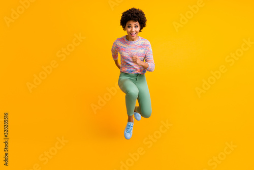 Full size photo of crazy dark skin curly lady jumping high rush fast discount shopping black friday low prices wear colorful pullover green pants shoes isolated yellow color background