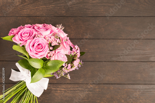 Bouquet of pink roses with white textile bow on brown wooden table. Copy space
