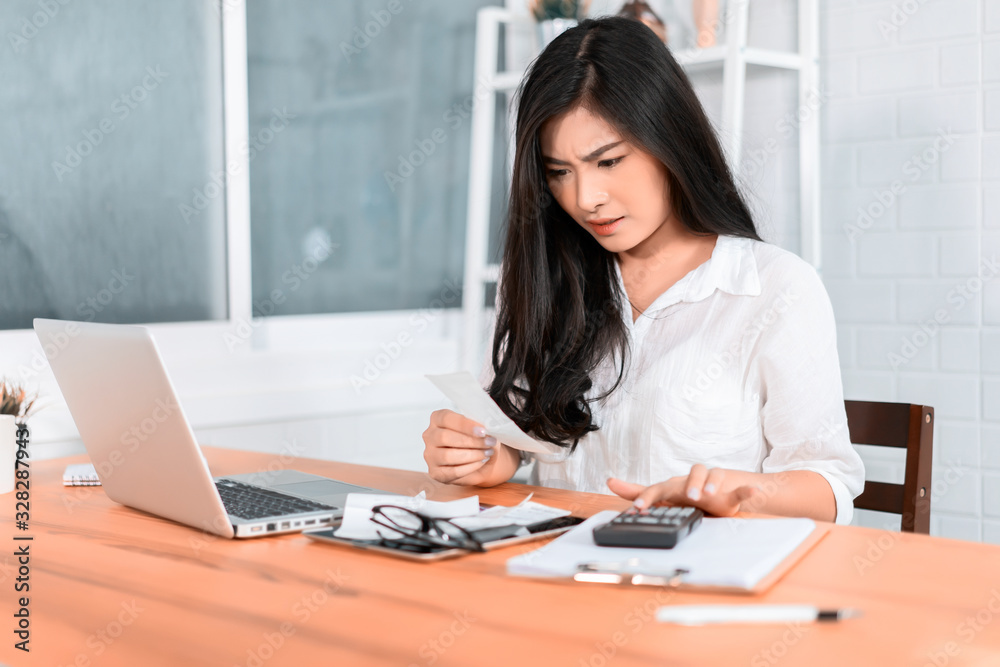 panic Asian woman checking expensive electricity and house hold bills, reads documents attentively, prepares financial report, calculates on laptop computer. finance interior,domestic housework panic Asian woman checking expensive electricity and house hold bills, reads documents attentively, prepares financial report, calculates on laptop computer. finance interior,domestic housework
