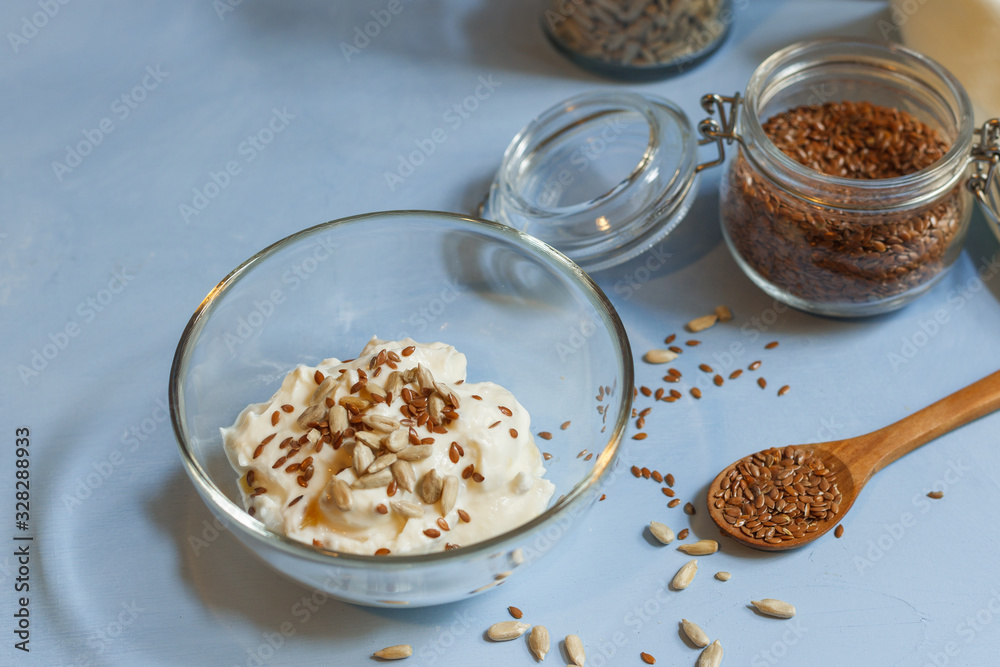 Soy yogurt with flax and sunflower seeds in a glass bowl on a blue background close-up