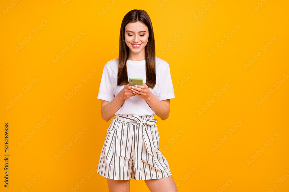 Photo of pretty attractive lady hold telephone hands reading e-mail friends party invitation wear casual white t-shirt striped summer shorts isolated vibrant yellow color background Photo of pretty attractive lady hold telephone hands reading e-mail friends party invitation wear casual white t-shirt striped summer shorts isolated vibrant yellow color background